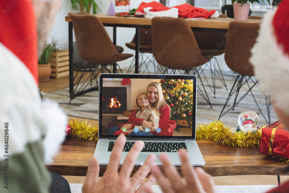 Naklejka premium Caucasian couple in santa hat on christmas video call on laptop with family