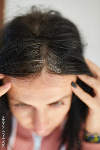 Portrait of a beautiful young woman examining her scalp and hair in mirror, hair roots, color, first grey hair, hair loss or dry scalp problem, or noticing that she is suffering from dandruff