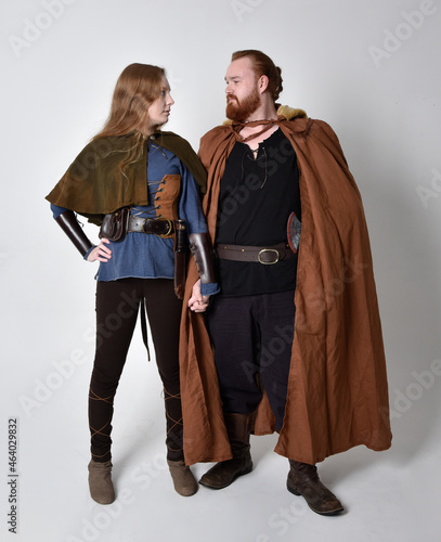 Full length  portrait of red haired  couple, man and woman wearing medieval viking inspired fantasy costumes, standing pose, isolated on white  studio background. 