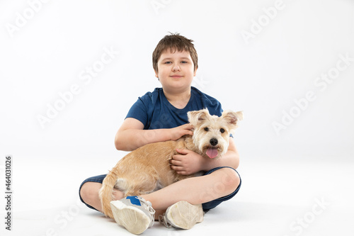 A young boy sits on a white background and in his hands he holds his beloved dog.