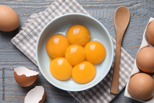 Chicken eggs and bowl with raw yolks on grey wooden table, flat lay