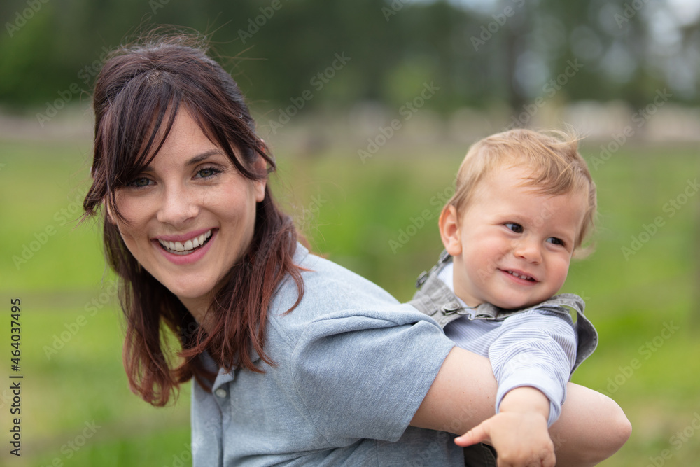 woman giving her infant child a piggy back outdoors woman giving her infant child a piggy back outdoors