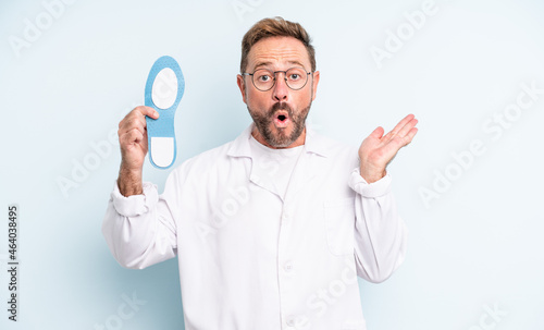 middle age handsome man looking surprised and shocked, with jaw dropped holding an object. podiatrist concept