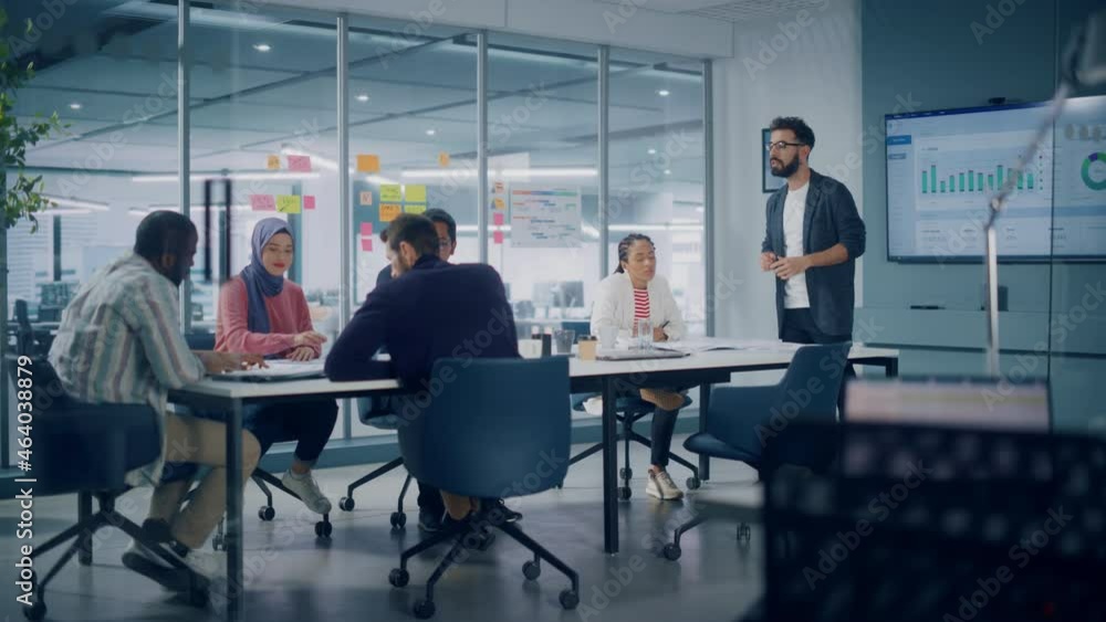 Diverse Modern Office: Businessman Leads Business Meeting with Managers, Talks, uses Presentation TV with Statistics, Infographics. Digital Entrepreneurs Work on e-Commerce Project. Moving Wide Shot Diverse Modern Office: Businessman Leads Business Meeting with Managers, Talks, uses Presentation TV with Statistics, Infographics. Digital Entrepreneurs Work on e-Commerce Project. Moving Wide Shot