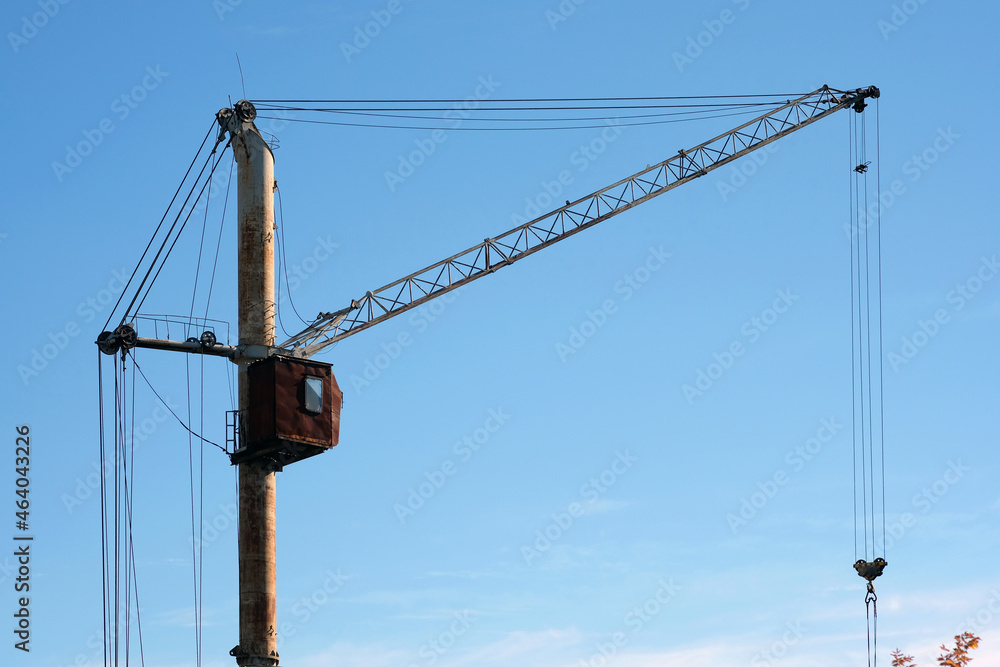 Old rusty construction crane against the background of the sky. Old style tower cranes abandoned on the outskirts of the city. Old rusty construction crane against the background of the sky. Old style tower cranes abandoned on the outskirts of the city.
