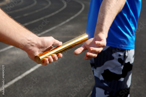 Man passing baton to his partner at stadium, closeup