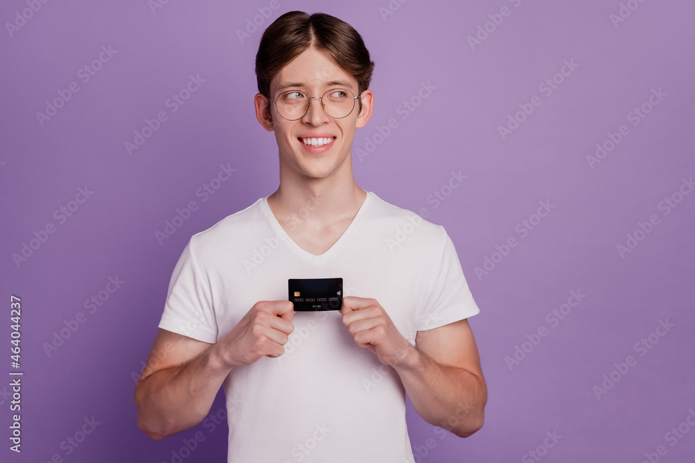 Photo of young cheerful man hold banking card wondered look empty space isolated on violet color background Photo of young cheerful man hold banking card wondered look empty space isolated on violet color background