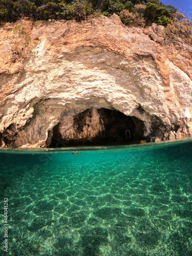 Underwater split photo of small white rock cave with crystal clear emerald sea and chapel of Agios Nikolaos built inside the cave, Desimi beach, Lefkada island, Ionian, Greece