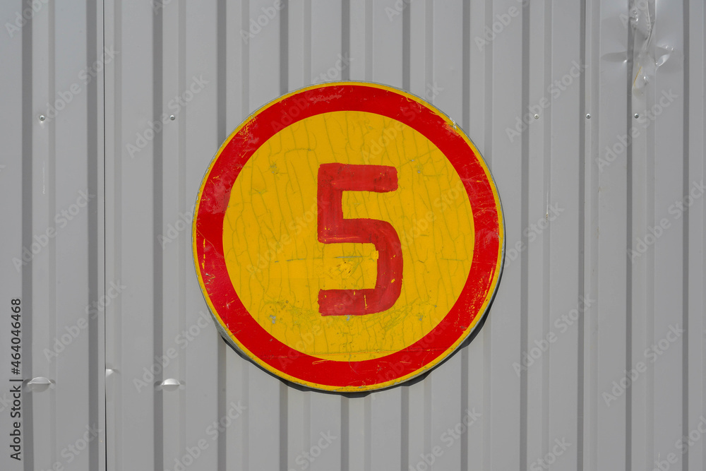 Photo of a gray fence on which a round red-yellow sign with the number 5 hangs Photo of a gray fence on which a round red-yellow sign with the number 5 hangs