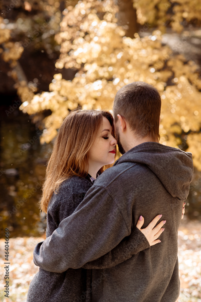 Fototapeta premium Beautiful young couple man and woman hugging in the park near the pond in leaf fall in autumn
