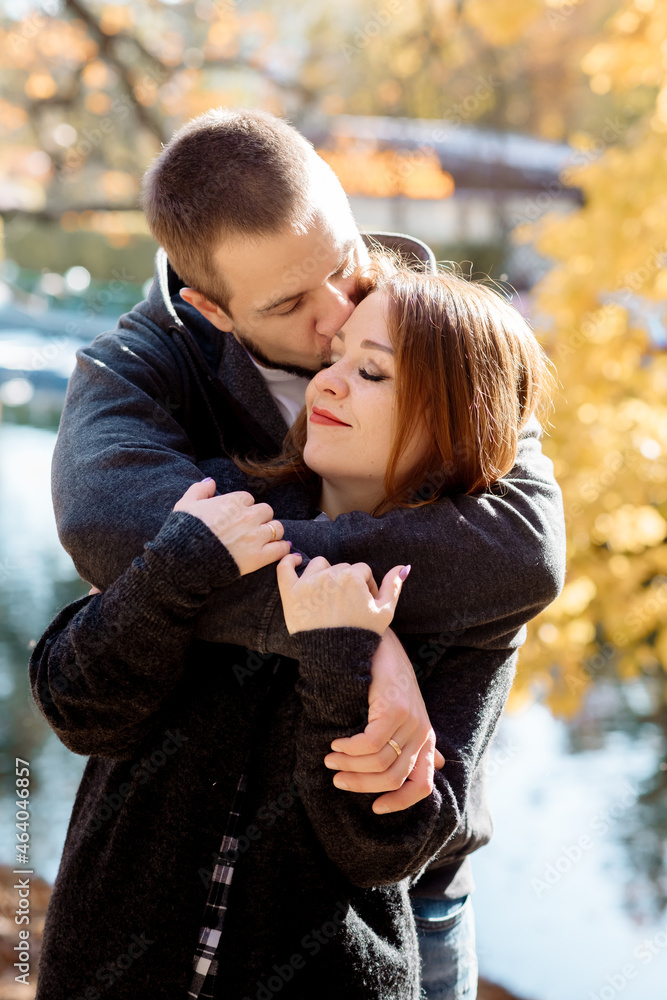 Fototapeta premium Beautiful young couple man and woman hugging in the park near the pond in leaf fall in autumn