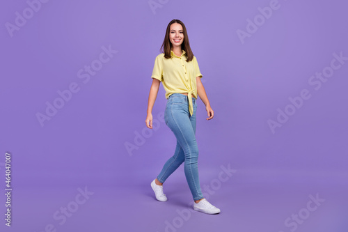 Full size photo of nice young brunette lady go wear yellow top jeans shoes isolated on purple color background