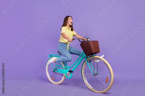 Full body profile photo of cool millennial brunette lady ride bicycle yell wear yellow top jeans sneakers isolated on violet color background © deagreez