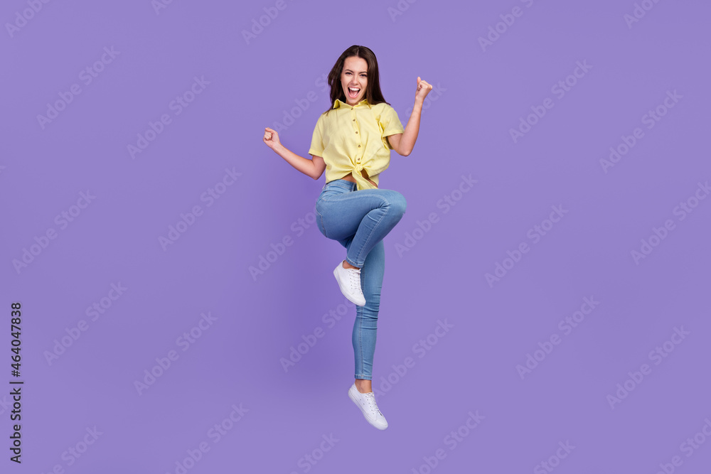 Full length photo of celebrate millennial brunette lady jump wear yellow top jeans sneakers isolated on violet color background