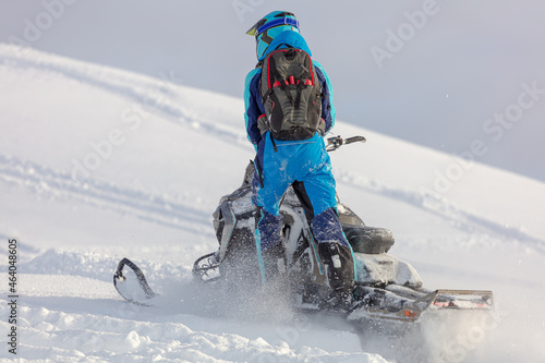 conquering the top on a mountain snowmobile with a body weight of one leg. snowmobiler harmoniously dressed in the color of a snow motorcycle