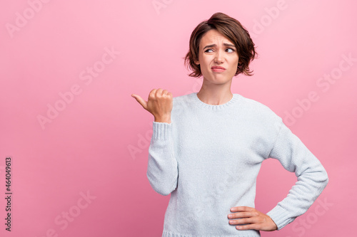 Photo of unhappy upset doubtful young woman point finger empty space thumb dislike isolated on pink color background