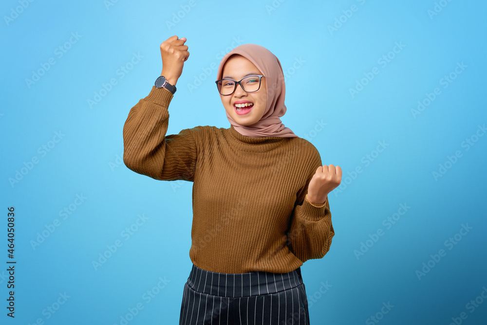 Fototapeta premium Portrait of cheerful beautiful Asian woman rejoicing celebrating luck on blue background