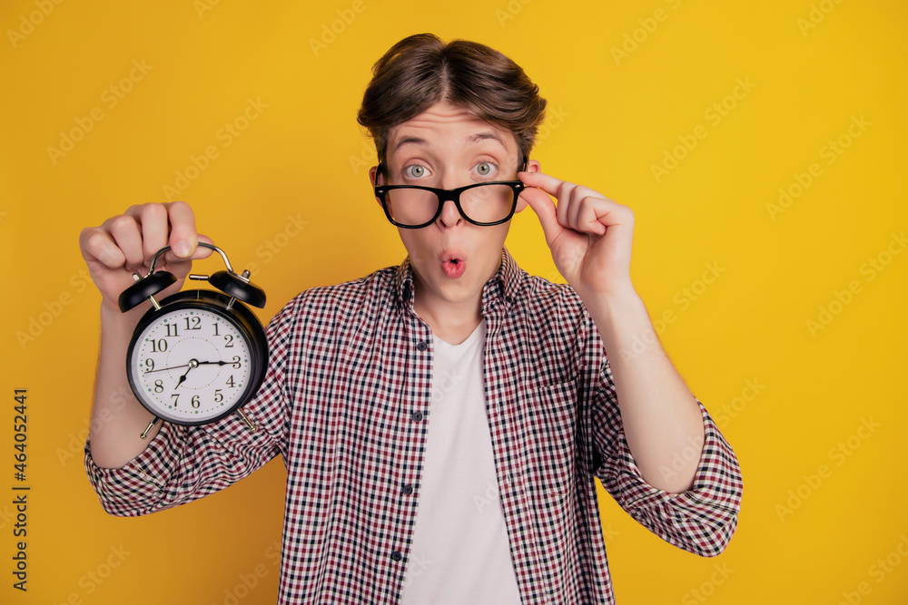 Photo of amazed shocked young man hold hands alarm oversleep morning late isolated on yellow color background Photo of amazed shocked young man hold hands alarm oversleep morning late isolated on yellow color background