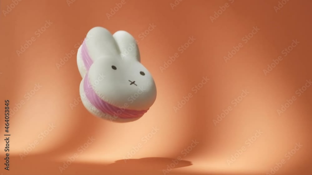Big White and Pink Spongy Rabbit falling down on the orange background. Hare-Shaped squishy Toy Bounces Off Orange Surface in Slow Motion. 500 fps Big White and Pink Spongy Rabbit falling down on the orange background. Hare-Shaped squishy Toy Bounces Off Orange Surface in Slow Motion. 500 fps