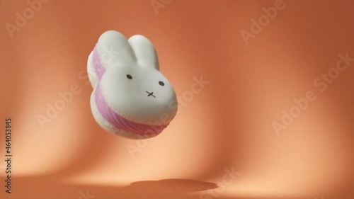 Big White and Pink Spongy Rabbit falling down on the orange background. Hare-Shaped squishy Toy Bounces Off Orange Surface in Slow Motion. 500 fps photo