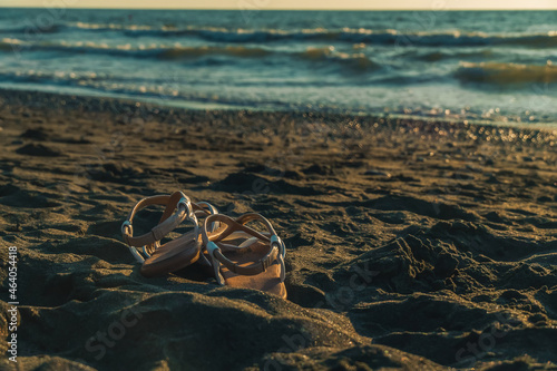 Close-up of leather sandals lying on the sand on the beach against the background of the sea with copy space. Beautiful background on the theme of travel, beach holidays