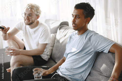 Male friends watching tv together in a bright room © hetmanstock2