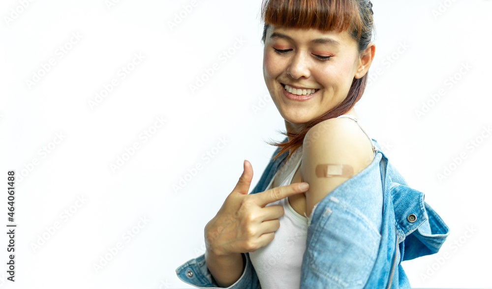 Asian woman smiling using adhesive bandage plaster at arm gesture after injection vaccine on a white isolated background. Female cheerful and confident in getting vaccinated against various diseases. - obrazy, fototapety, plakaty 