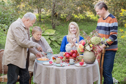happy family at laid table with apple pie in garden