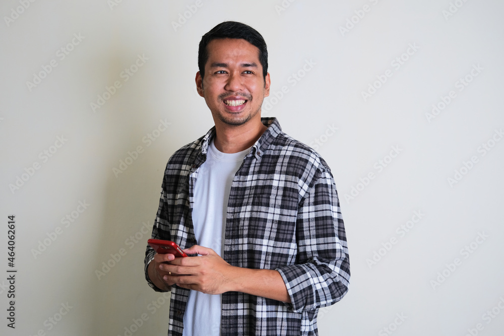 Adult Asian man standing confident while holding mobile phone Adult Asian man standing confident while holding mobile phone