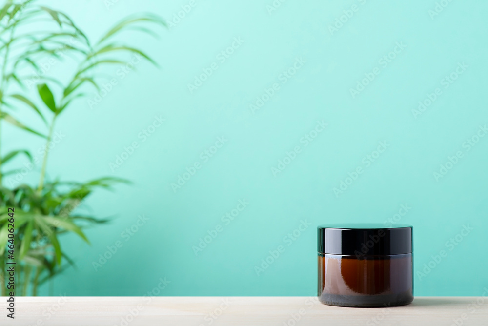 Amber glass jar for cream or lotion. Skincare concept on mint and wooden surface background with green palm leaves. Spa natural cosmetic concept for face body care Amber glass jar for cream or lotion. Skincare concept on mint and wooden surface background with green palm leaves. Spa natural cosmetic concept for face body care