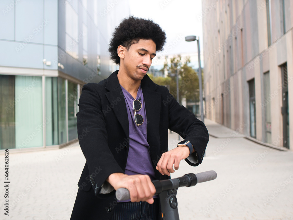 Confident ethnic man checking time on smartwatch standing on scooter on street Confident ethnic man checking time on smartwatch standing on scooter on street