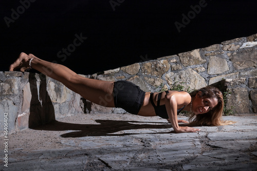 blonde woman dressed in black doing push-ups at night with her feet on a wall