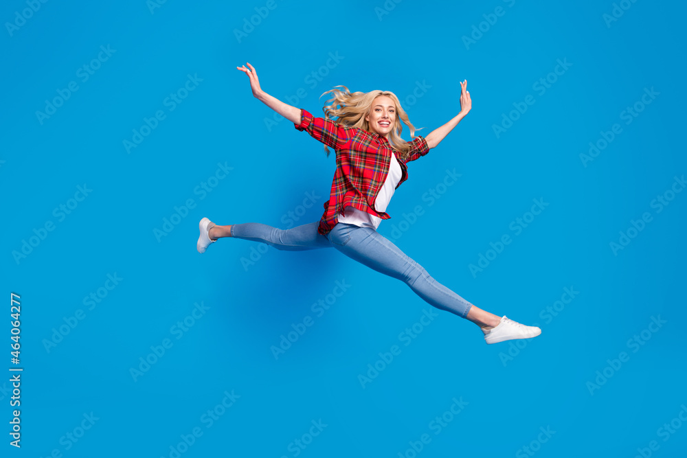 Photo of pretty adorable young lady wear plaid shirt smiling jumping high legs hands arms sides isolated blue color background