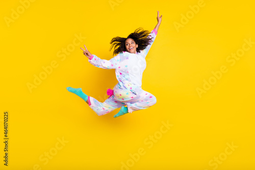 Full length body size view of beautiful trendy cheerful girl jumping showing v-sign isolated over bright yellow color background