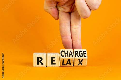 Relax and recharge symbol. Businessman turns cubes and changes the word 'relax' to 'recharge'. Beautiful orange table, orange background. Business, relax and recharge concept. Copy space.