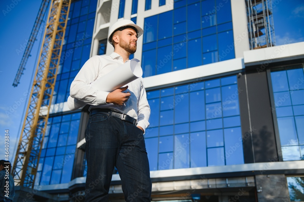 Successful engineer or architect, crane and building construction at backgrpound. Joyous businessman wearing helmet Successful engineer or architect, crane and building construction at backgrpound. Joyous businessman wearing helmet