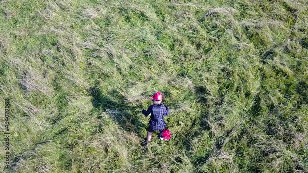 Teenage boy trying to mow tall overgrown grass in a meadow with a powerful petrol string trimmer - brushcutter. Above view Teenage boy trying to mow tall overgrown grass in a meadow with a powerful petrol string trimmer - brushcutter. Above view