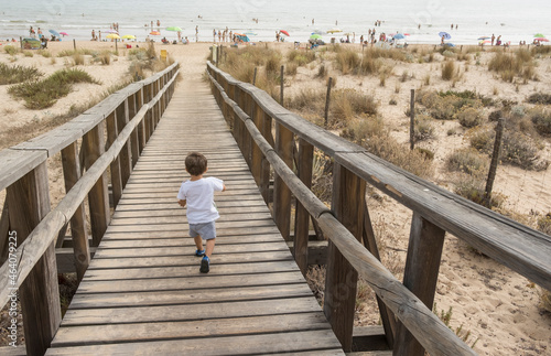Young little boy running to the beach on wooden walkway
