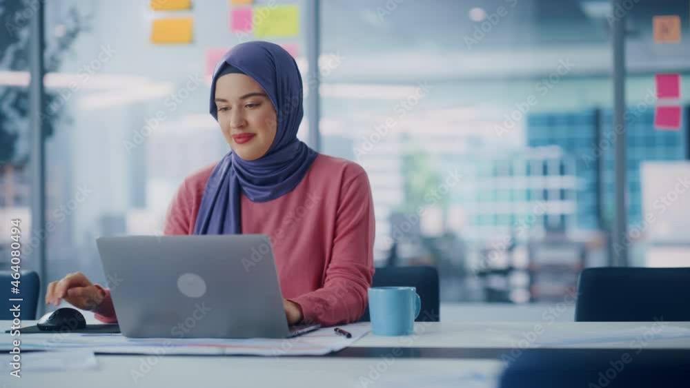 Modern Office: Portrait of Young Muslim Businesswoman Wearing Hijab Works on Laptop, Does Data Analysis, Website Design, Creative Development. Digital Entrepreneur Works on e-Commerce Startup Project Modern Office: Portrait of Young Muslim Businesswoman Wearing Hijab Works on Laptop, Does Data Analysis, Website Design, Creative Development. Digital Entrepreneur Works on e-Commerce Startup Project