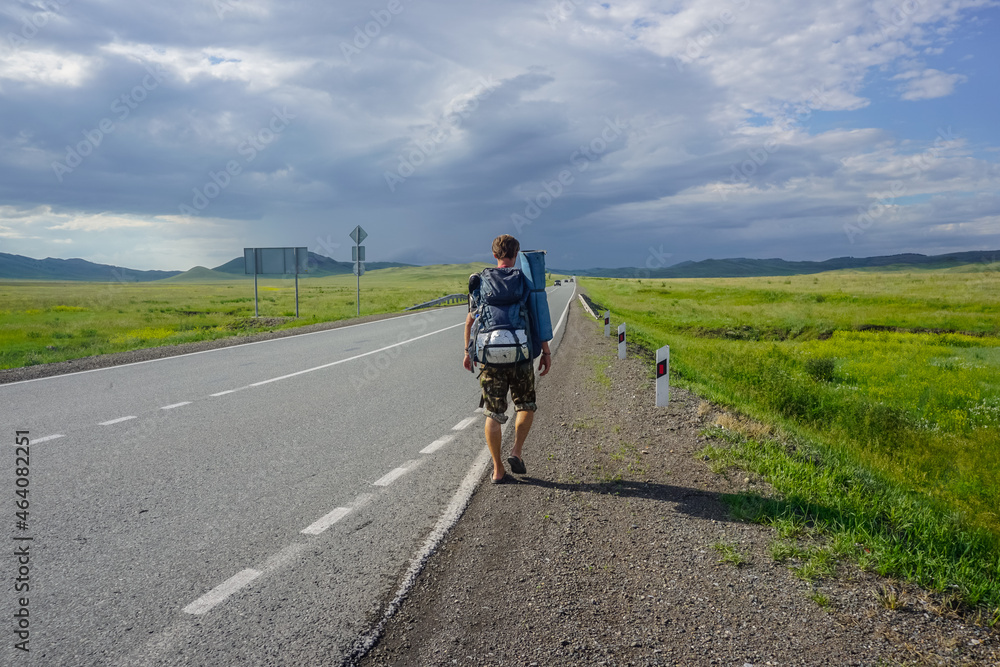 Traveler with a backpack walks along the road