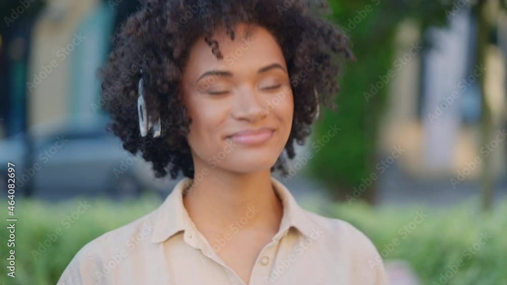 Happy biracial woman with curly hair putting headset on and walking urban street Happy biracial woman with curly hair putting headset on and walking urban street