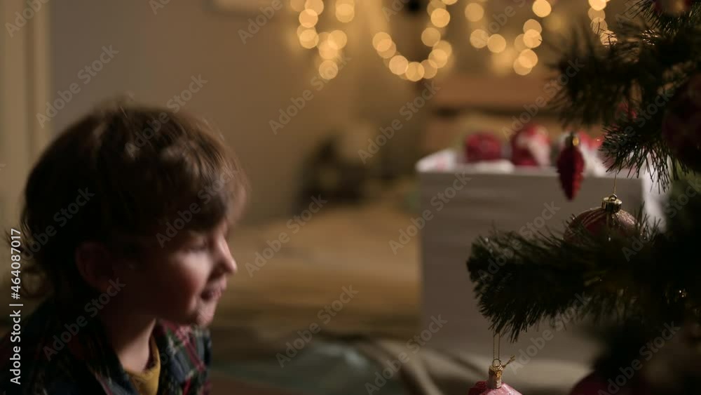 Christmas tree. A little boy at night at home plays with Christmas tree decorations, hangs a beautiful toy on a spruce branch. The mischievous kid is happy and smiling, he likes Christmas. Christmas tree. A little boy at night at home plays with Christmas tree decorations, hangs a beautiful toy on a spruce branch. The mischievous kid is happy and smiling, he likes Christmas.