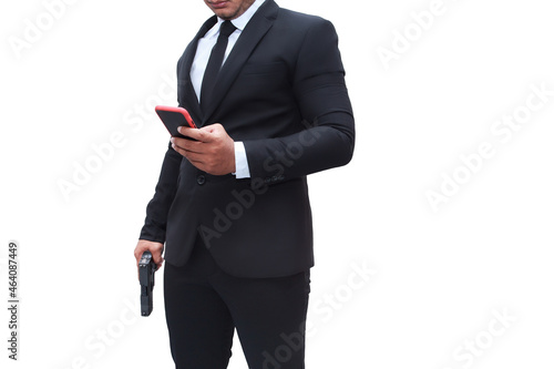 A gun man in black suit is holding a pistol and his other hand is going to his mobile to check his target on a white background isolated mission. Concept for assassin, murder, criminal, thief. photo