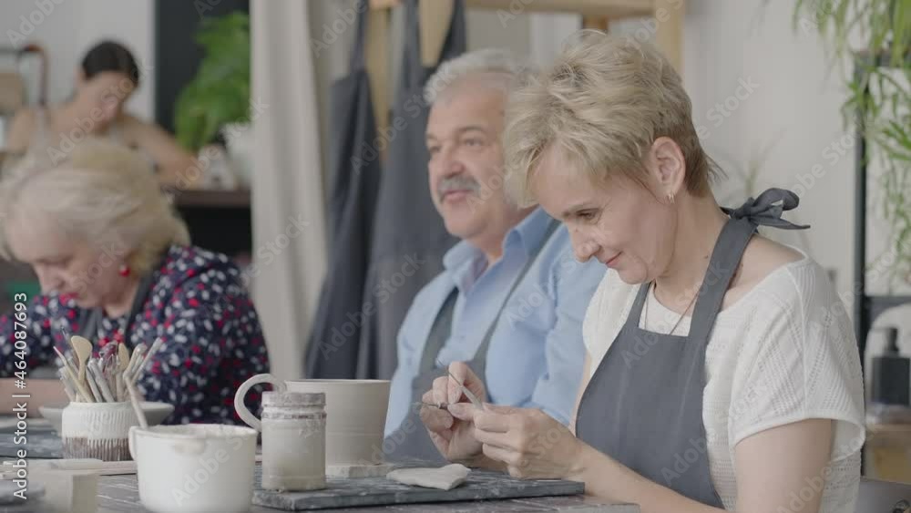 A group of elderly people at a master class in pottery together sculpt and cut a drawing on cups of clay for the manufacture of ceramic dishes A group of elderly people at a master class in pottery together sculpt and cut a drawing on cups of clay for the manufacture of ceramic dishes