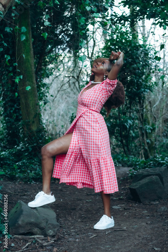 Beautiful African black woman in park. Beautiful young woman with brown skin. Smiling black woman with afro hair wearing pink gingham dress and pearls.