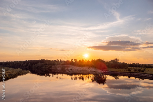 Colorful sunset over the river in the countryside. Drone photo of burning sun reaching the horizon with a huge calm river on the foreground