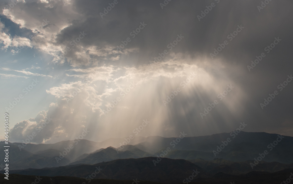 Sunbeams breaking through clouds onto mountains below - horizontal