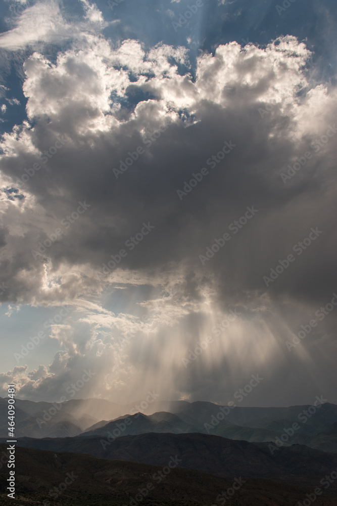 Obraz premium Sunbeams breaking through clouds onto mountains below - vertical