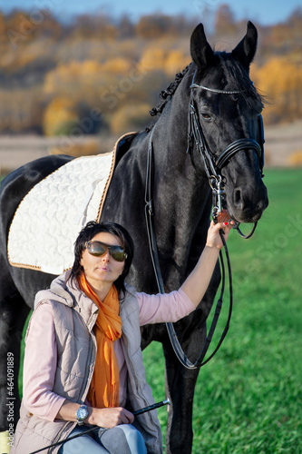 portrait of beautiful black horse with his owner and rider posing in green grass meadow. autumn season