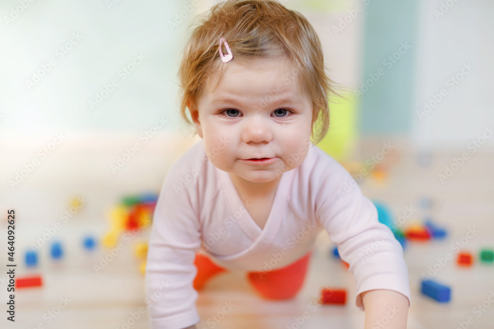 Cute little baby girl playing with educational toys. Happy healthy child having fun with colorful different wooden blocks at home or nursery. Baby crawling and learning colors and forms, indoors Cute little baby girl playing with educational toys. Happy healthy child having fun with colorful different wooden blocks at home or nursery. Baby crawling and learning colors and forms, indoors